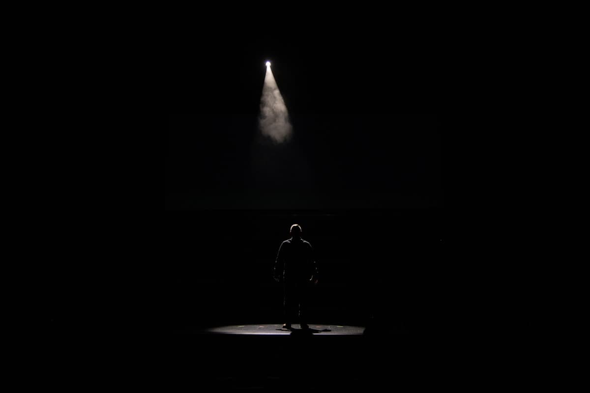A person standing alone in a spotlight on a dark stage